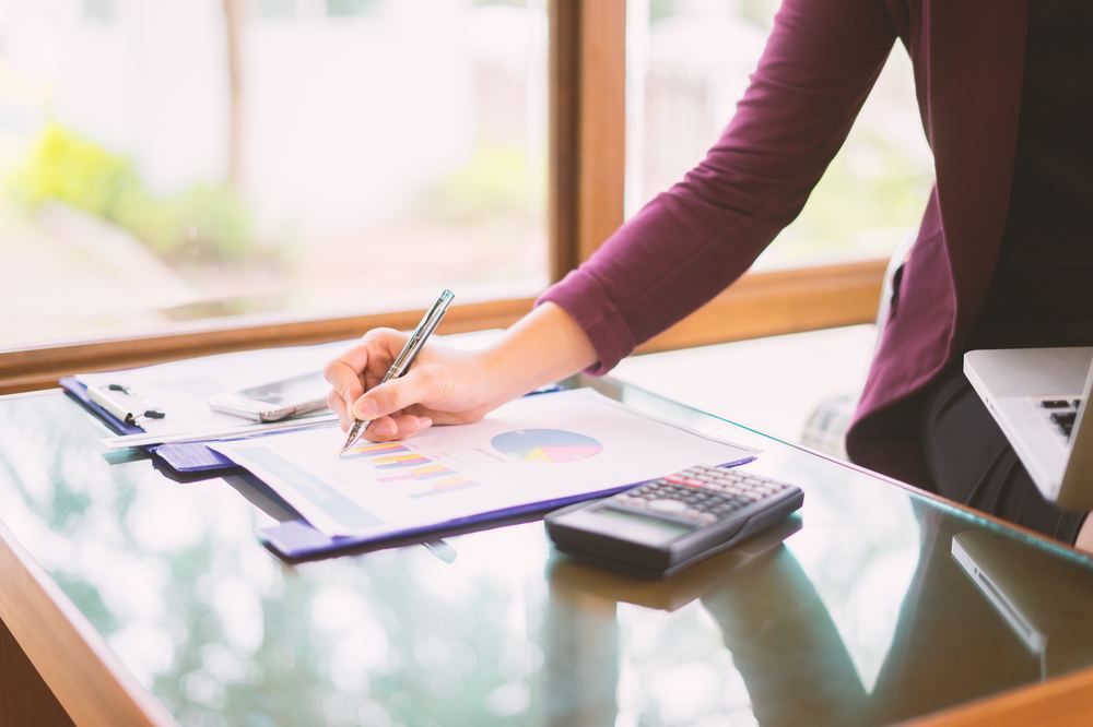 Mulher analisando gráficos financeiros com calculadora, representando o planejamento patrimonial