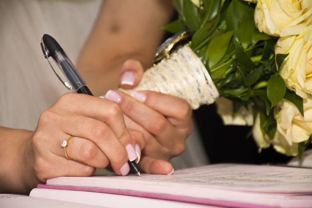Noiva assinando o registro de casamento, com buquê de flores ao lado, representando o ato de casar cuja validade pode ser questionada