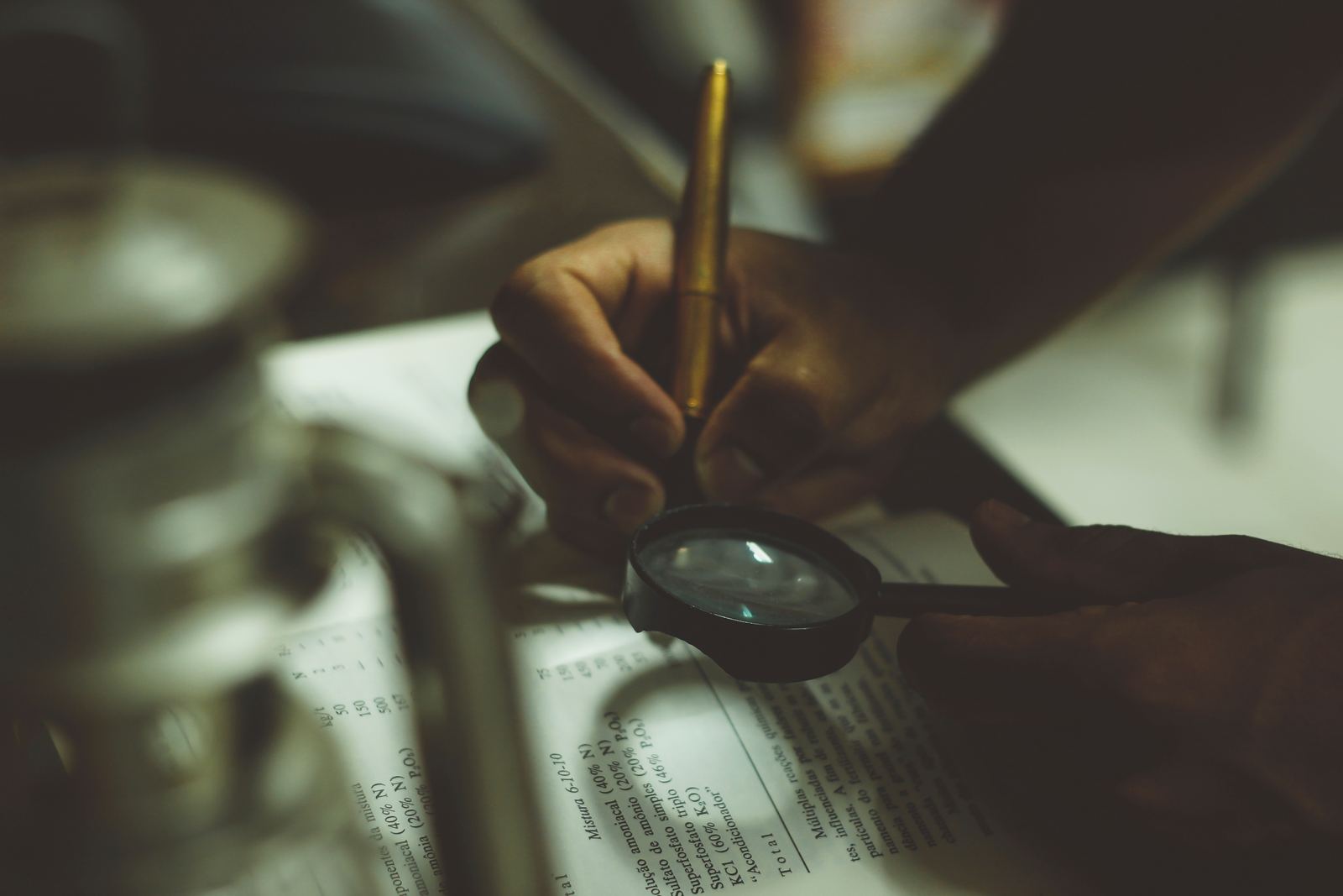 Mãos segurando uma lupa sobre um documento, representando a análise de um pedido de mudança de nome