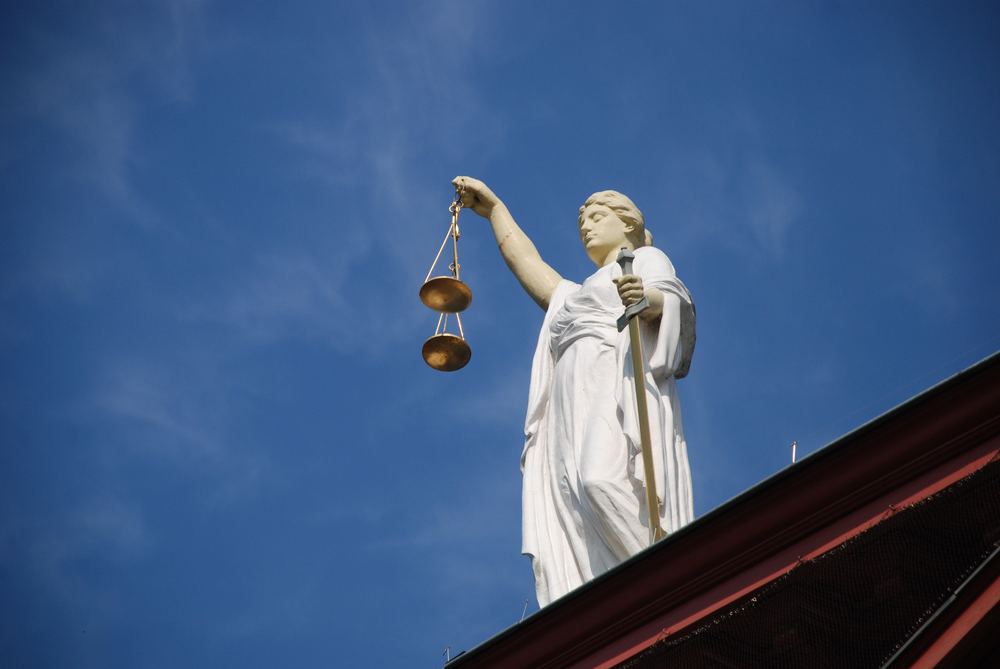 Estátua da Justiça segurando a balança contra o céu azul, no alto de um prédio