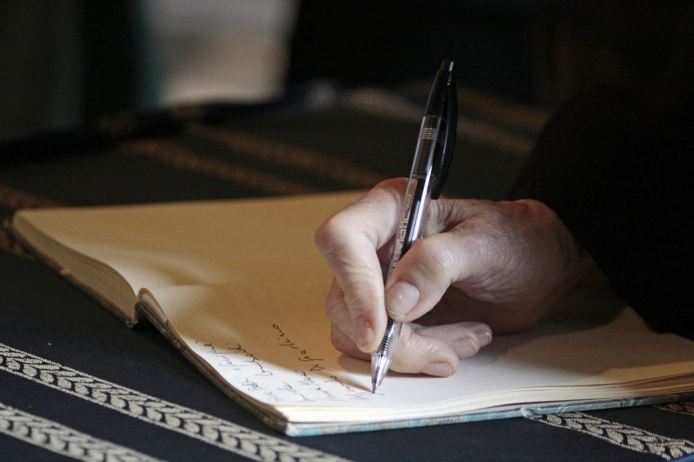 Mão de uma pessoa idosa escrevendo em um caderno, representando o vínculo entre avós e netos