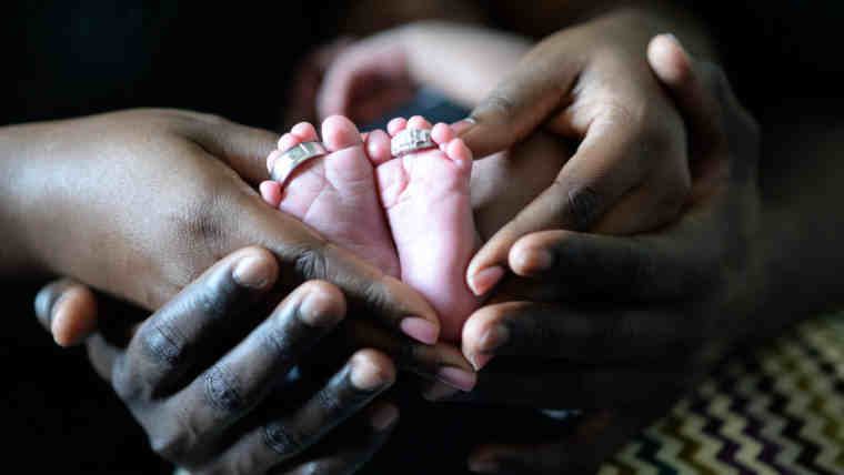 Mãos dos pais segurando os pezinhos de um bebê recém-nascido, representando o vínculo de paternidade